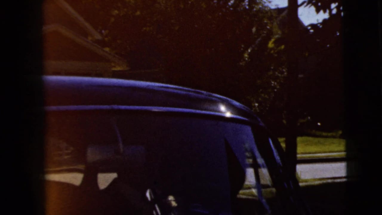 1962 Moline frame of a classic car side and windshield area, with the vehicle partly in shadow near trees.