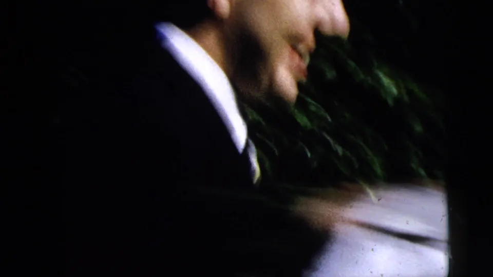 1962 Moline home-movie frame showing a smiling suited man near a car window during a formal occasion.