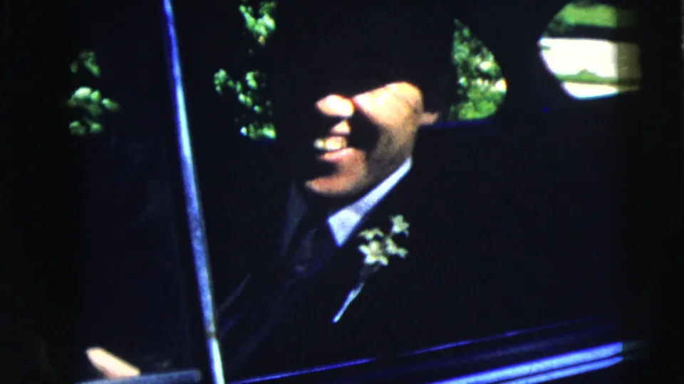1962 Moline frame showing a smiling man in a dark suit with a white corsage seated inside a classic car.
