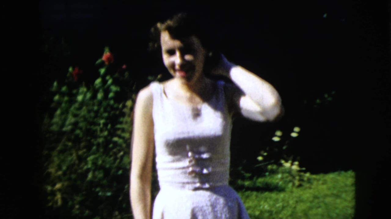 Young woman in a white sleeveless dress smiles in a sunny yard.