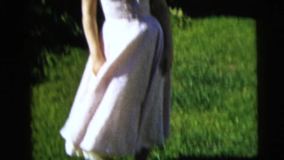 A fuller view shows the young woman in a white dress standing on a green lawn in 1962 Moline home-movie footage.