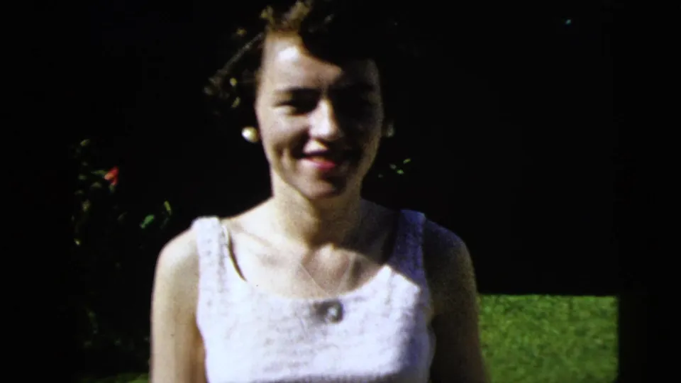 A smiling young woman in a white sleeveless dress and pearl earrings fills more of the 1962 Moline garden frame.
