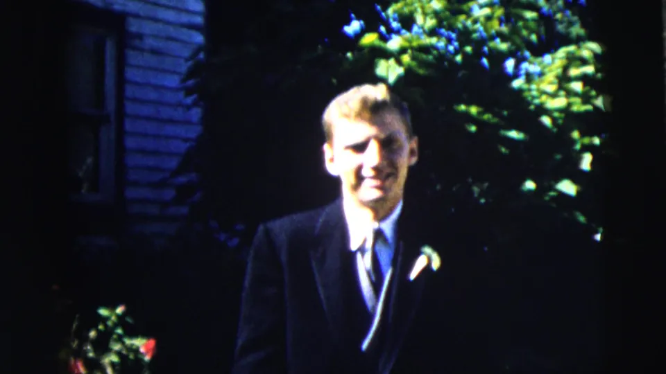 The young man faces the camera in a dark suit and boutonniere, framed by foliage outside a Moline residence in 1962.