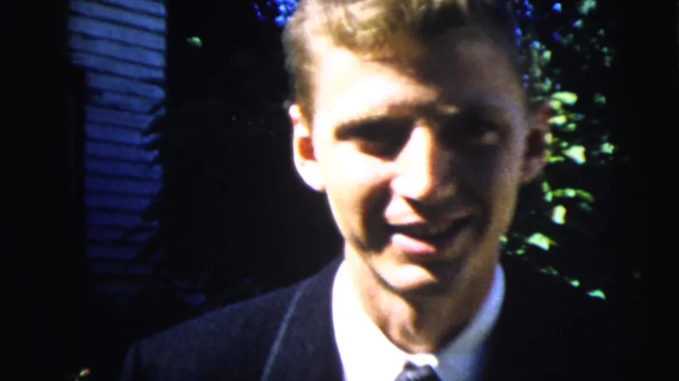 A close 8mm view shows the young man smiling in suit and tie, with strong sun and shadow across his face in Moline, Illinois footage.