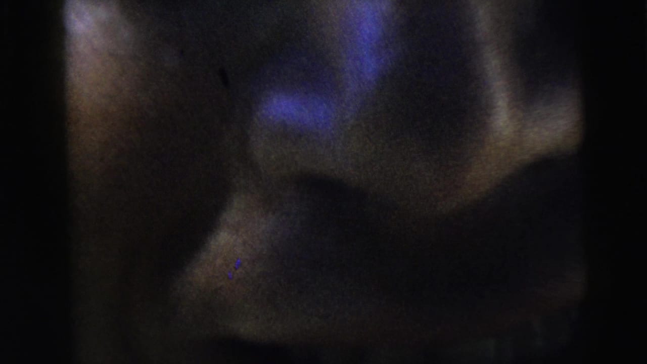 Shadowed close-up of a man's face with mouth open in blue-black light.