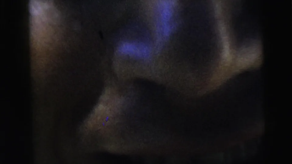 1962 Moline home-movie frame showing a man's partially visible face in darkness with his mouth open and blue light across his features.
