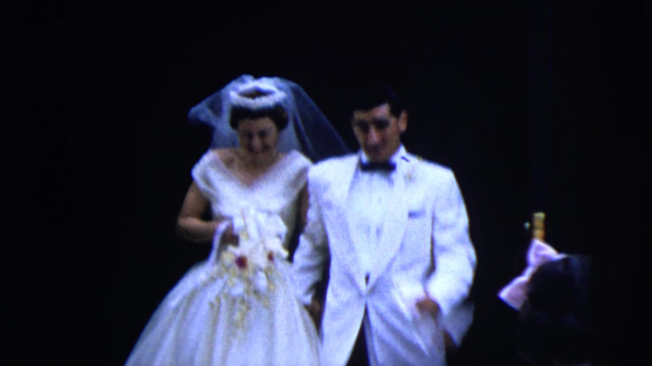 Bride and groom in formal wedding attire walk out from a dark doorway.