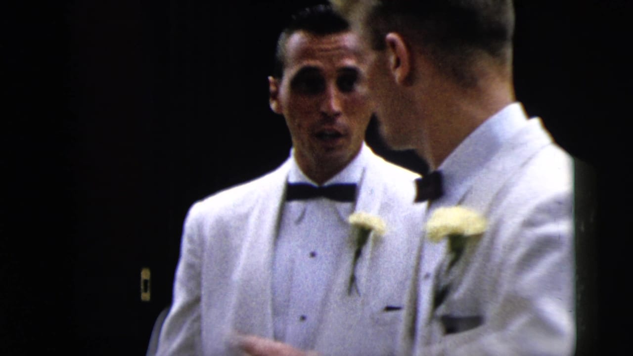 1962 Moline frame of men in white dinner jackets with boutonniere flowers conversing during a formal arrival.