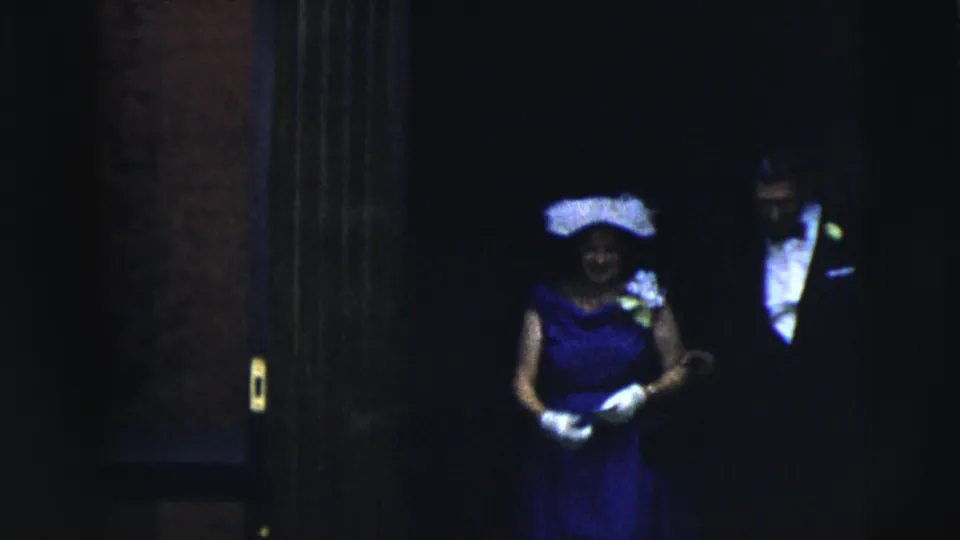 1962 Moline formal-event frame showing a woman in a blue gown, light hat, and gloves entering a dim venue.
