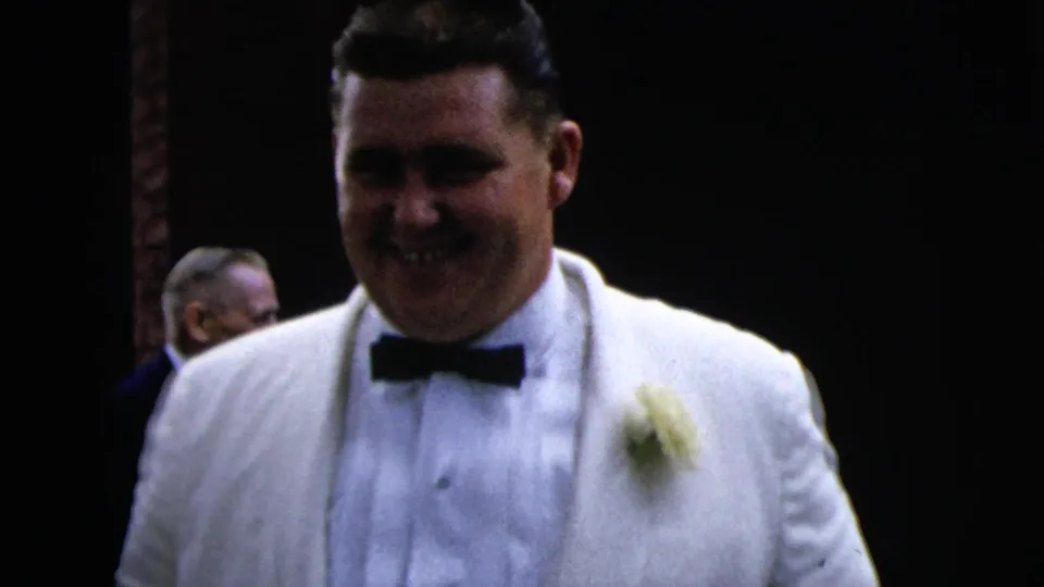 A smiling man in a white tuxedo and black bow tie stands close to the camera during a 1962 Moline formal event.