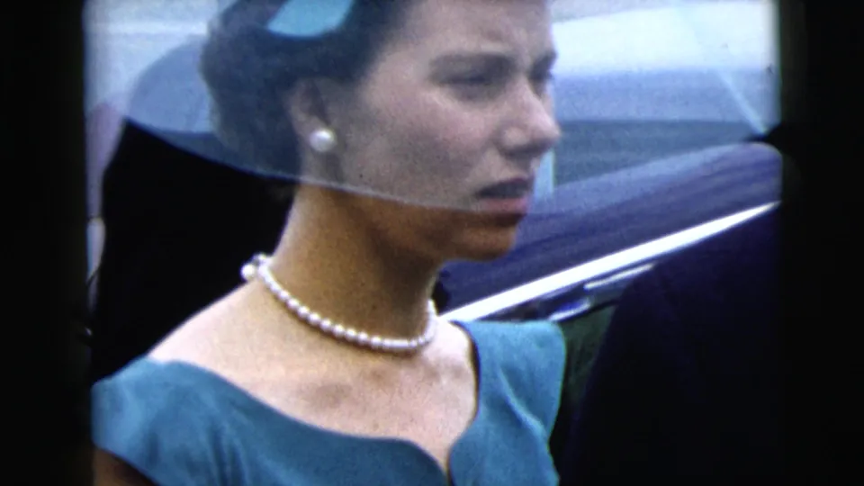 A woman in a blue dress, pearl necklace, and sheer veil or headpiece appears in profile near a car in Moline, Illinois, 1962.