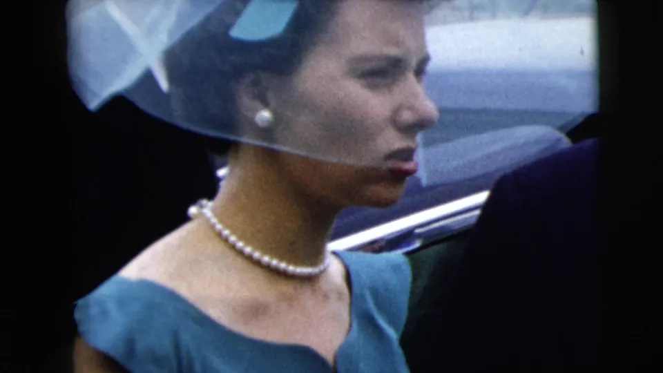 The woman in blue remains in side profile, wearing pearls and a sheer headpiece beside a car at the 1962 Moline gathering.