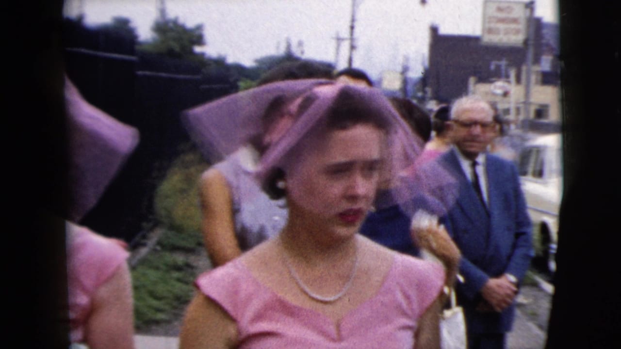 A pink-dressed bridesmaid with a matching veil and pearl necklace moves through an outdoor wedding crowd in 1962 Moline footage.