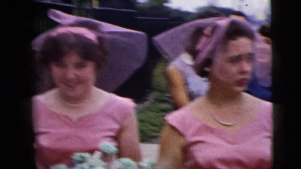 Two bridesmaids in matching pink formalwear appear in soft-focus 8mm footage during a Moline wedding procession.