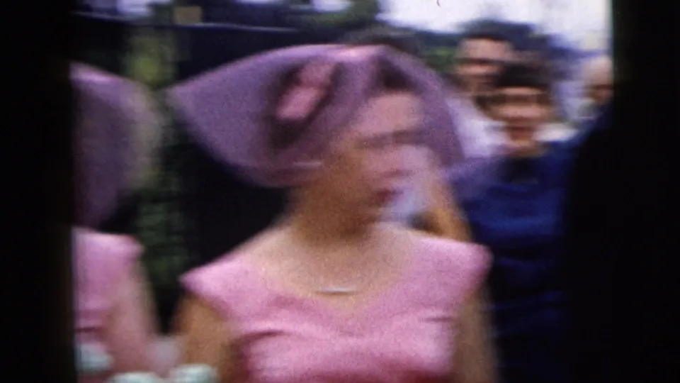 Motion-blurred 8mm frame of a pink-clad bridesmaid passing wedding guests outdoors in Moline, Illinois, in 1962.