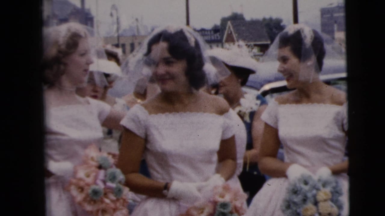 Bridal party members in white and pale dresses gather on a Moline street, smiling and holding bouquets with other adults nearby.