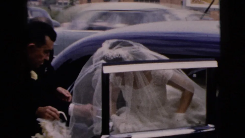 In Moline, Illinois, 1962, a veiled bride begins stepping out of a blue car as a suited man stands at the door.