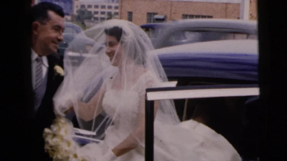 In Moline, Illinois, a bride in a white veil exits a car as the groom stands nearby during a 1962 wedding scene.