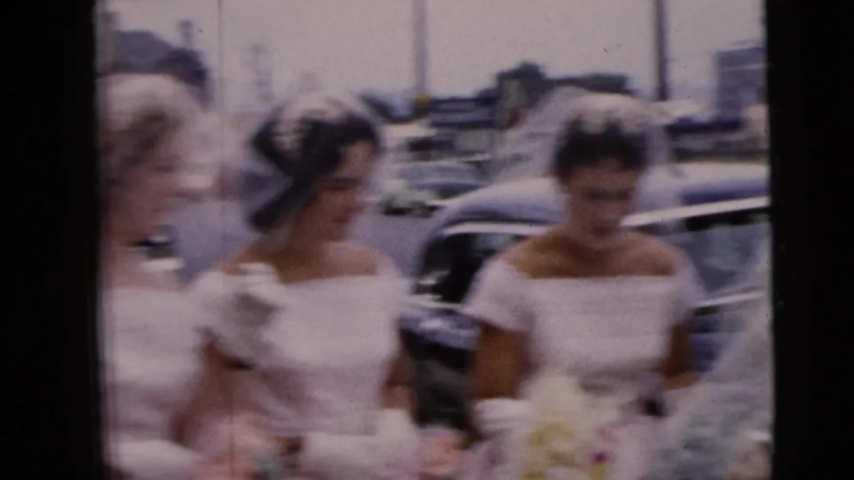 Women in pale formal dresses pass near the veiled bride, with parked cars and city buildings visible in Moline, Illinois.