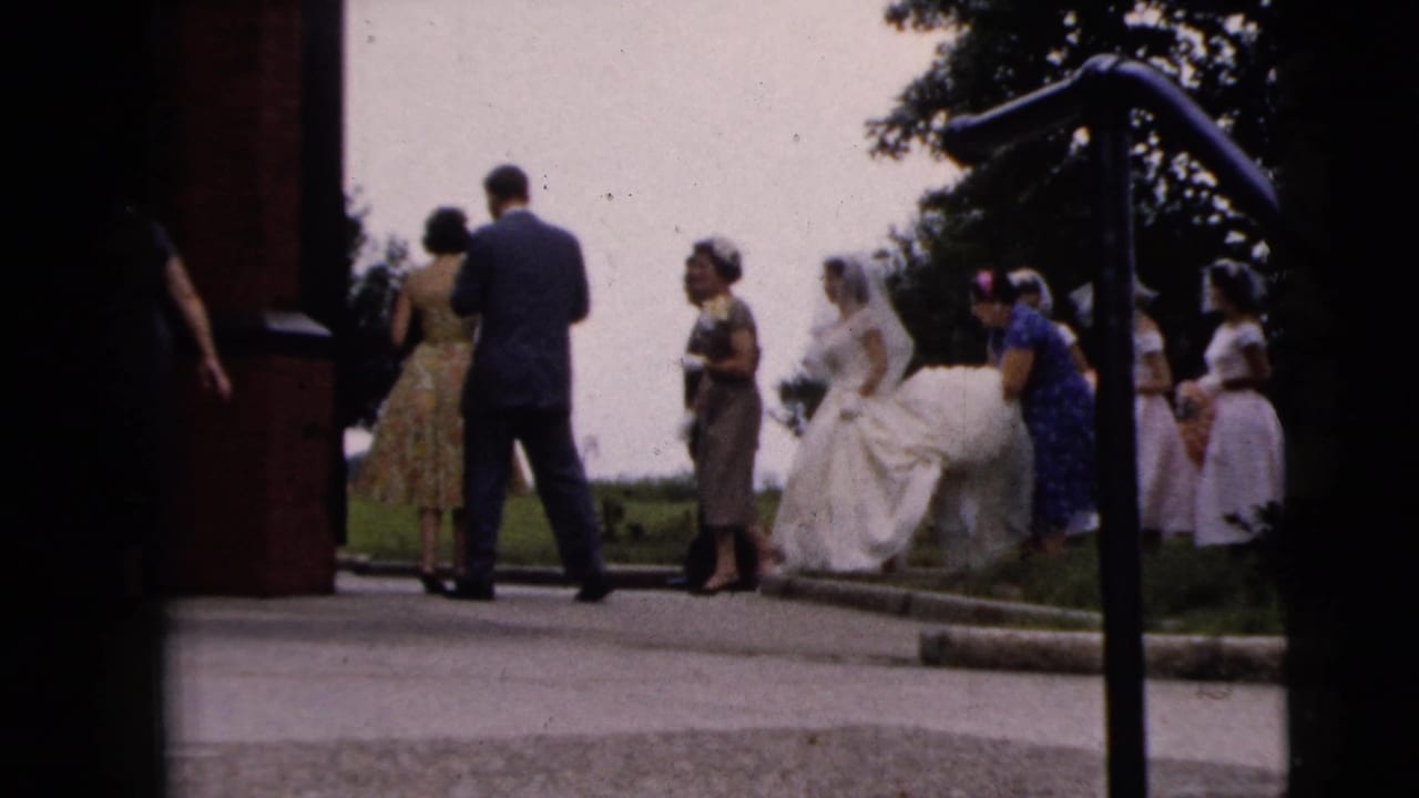 Wedding party gathers outside a building entrance near steps and a railing.