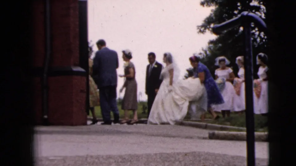 A woman in blue appears to assist the bride's train while attendants wait outside the entrance in 1962 Moline.
