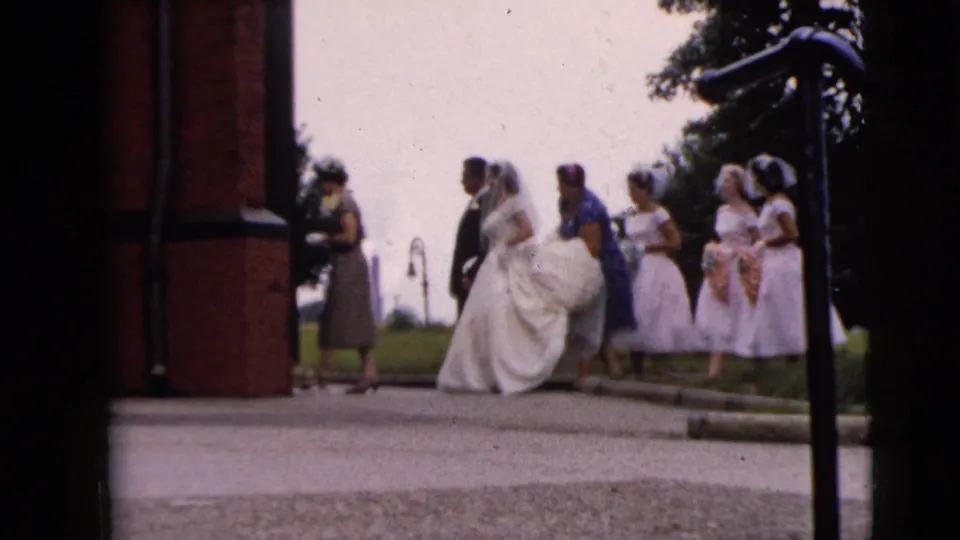 The wedding party continues toward the entrance, with the bride's full skirt, veils, and pastel dresses visible.