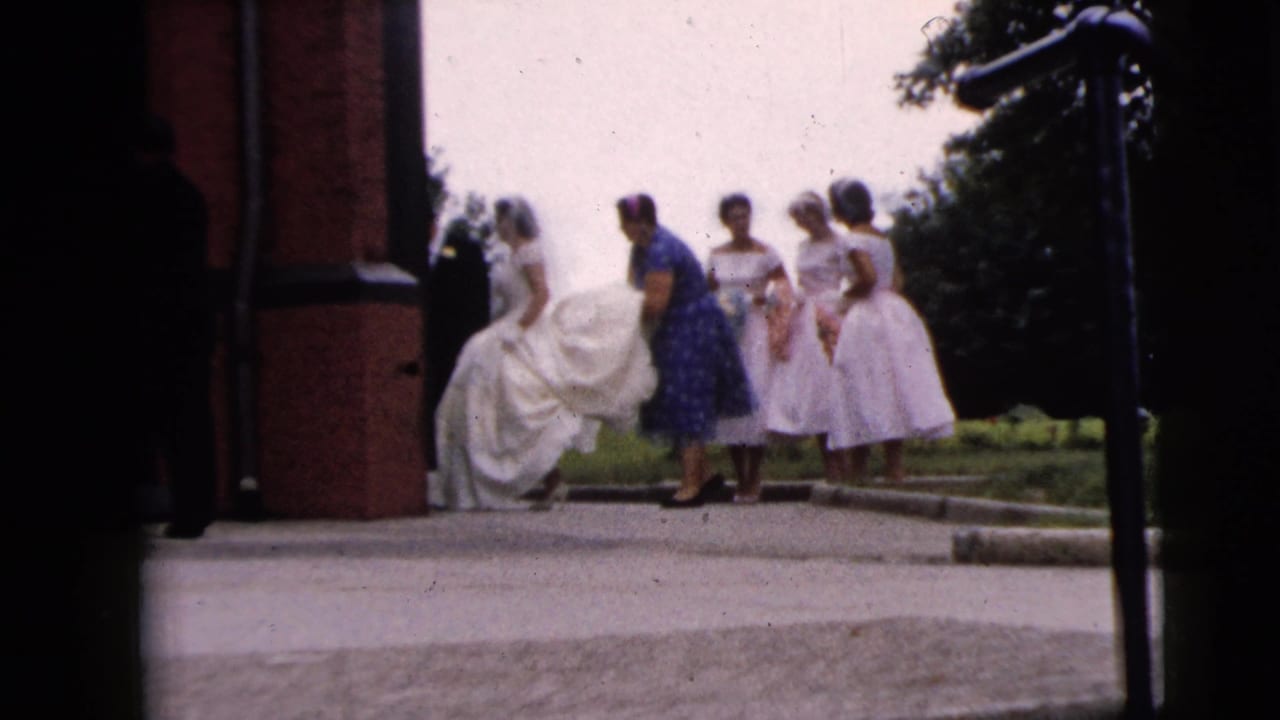 1962 Moline, Illinois 8mm frame showing a bride in a white gown with women in pastel dresses near a brick church entrance.