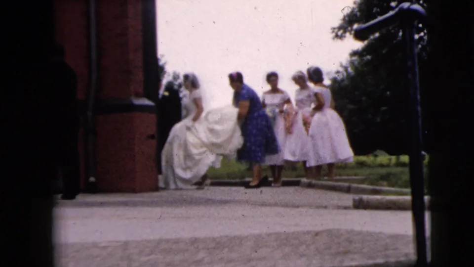 1962 Moline, Illinois 8mm frame showing a bride in a white gown with women in pastel dresses near a brick church entrance.
