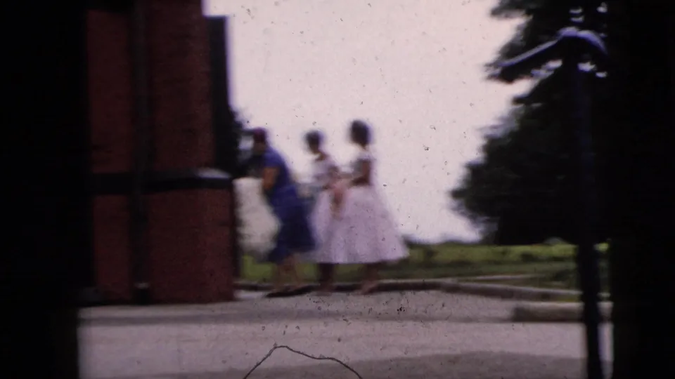 The bridal party appears in motion blur near the church entrance, with dresses and trees visible in the 1962 Moline home movie frame.