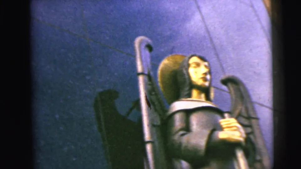 Low-angle 1962 home-movie view of the Moline angel statue, showing the halo, wings, torso, and sword held in front.