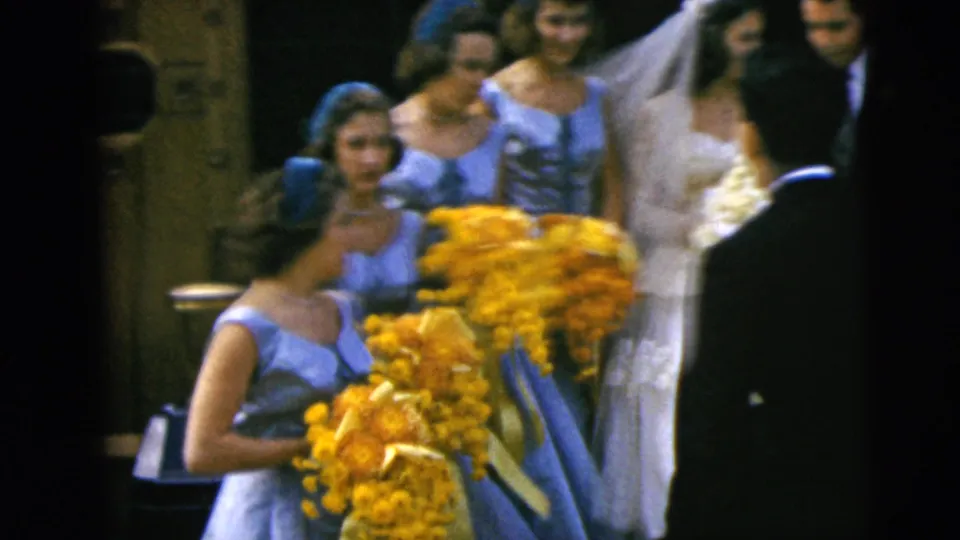 1962 Moline wedding party indoors, with bridesmaids in light blue dresses holding yellow bouquets near the bride and groom.