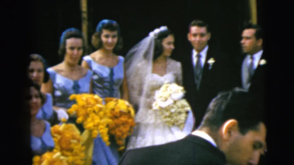 Bride and groom stand among bridesmaids in light blue dresses and ushers during a 1962 indoor wedding portrait moment.