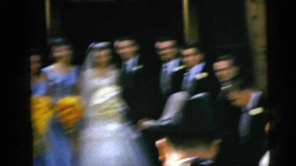 Soft, blurred 8mm frame of the 1962 Moline wedding party, with attendants and suited men visible around the bride and groom.