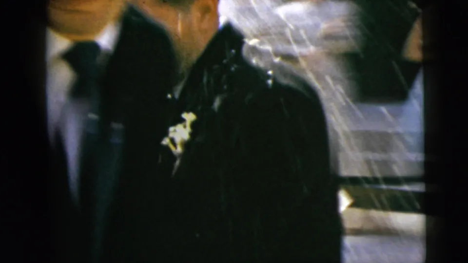 A closer 8mm view catches the bride and groom from the side, emphasizing the veil, dark suit, boutonniere, and soft motion blur.