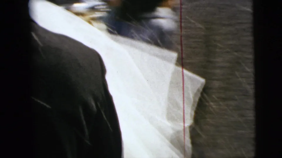 The final frame shows a close, partly blurred view of bridal fabric and a dark suit, likely as the camera passes near the couple.
