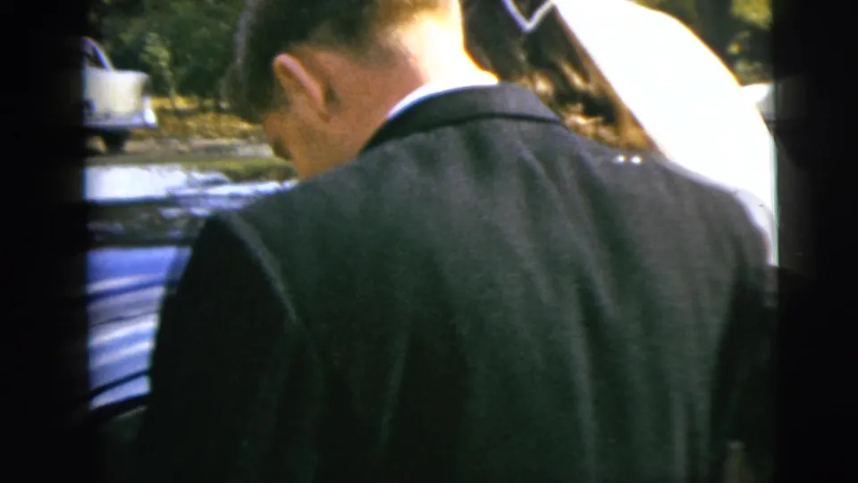 The groom stands at the side of a blue car during the 1962 Moline wedding departure, with the bride or attendant partly visible.