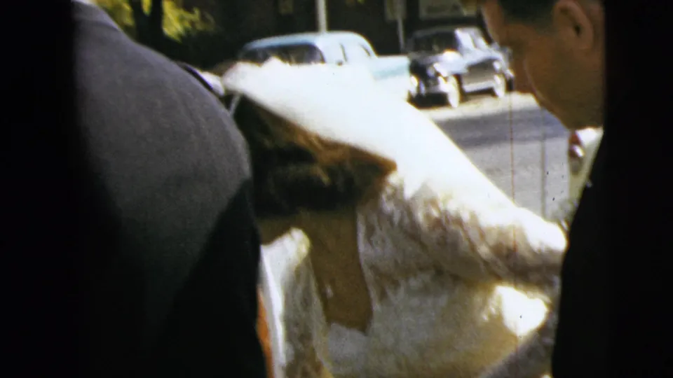 The bride in a lace gown leans near the car as a white-gloved attendant helps manage her dress in the Moline wedding scene.