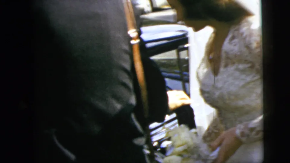 The bride and groom are framed beside the blue car door, with bridal lace, bouquet, and formal suits visible in the 1962 wedding footage.