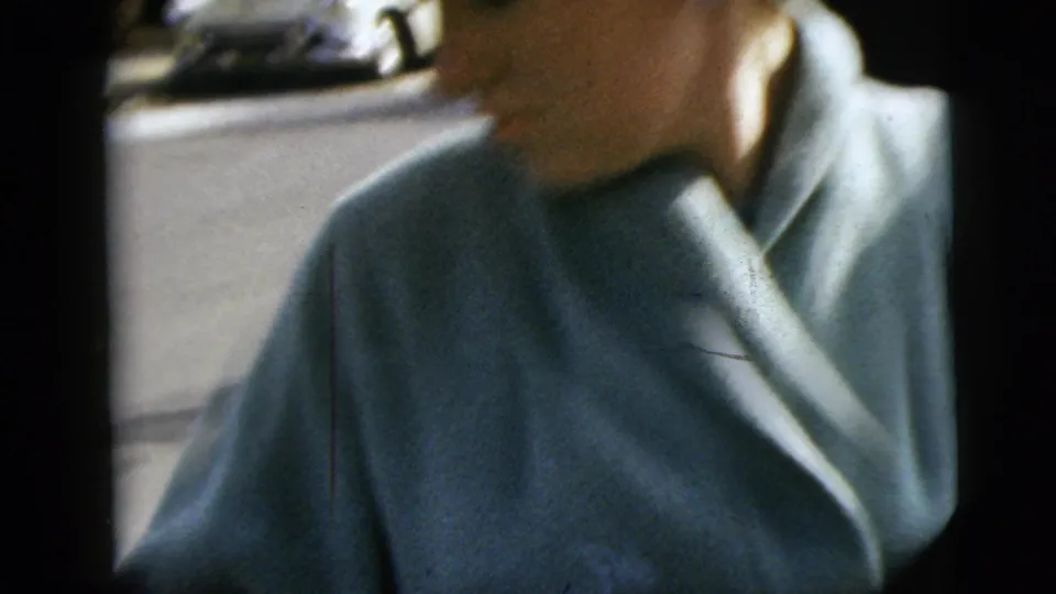 A woman in a pale blue coat moves close to the 8mm camera on a Moline street after the wedding departure moment.