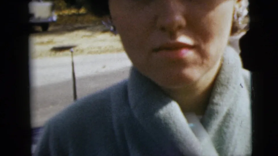 Close handheld view of a woman in a pale coat near the camera, with Moline street and sidewalk visible behind her.