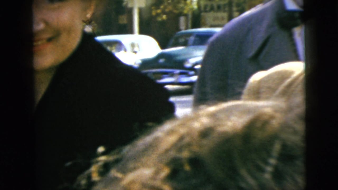Smiling woman near a car window with another adult and street traffic behind her.