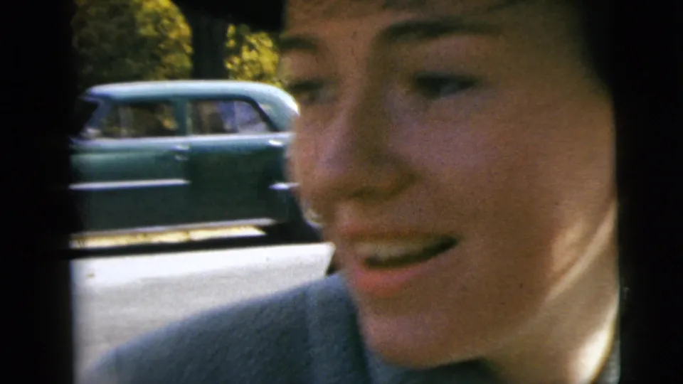 A woman in profile smiles inside or beside the car, with a classic station wagon passing along the Moline street behind the window frame.