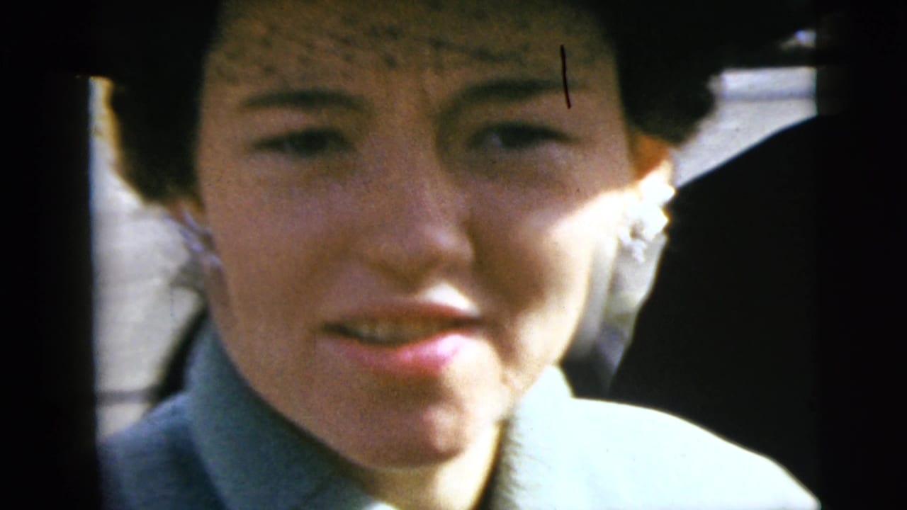 A woman in a pale coat and dark hat looks toward the camera from a car during 1962 home-movie footage in Moline, Illinois.