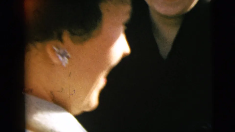 Close handheld 8mm view of a bride in profile on a wedding day, with another formally dressed person partly visible beside her.