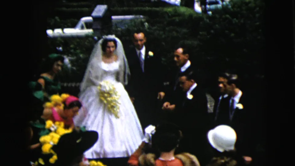Bride, groom, and wedding attendants remain posed outdoors in Moline, Illinois, with yellow flowers and guests visible around them.