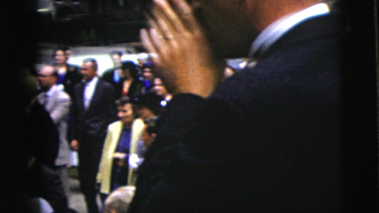 Guests in formal clothing stand near a crowded wedding ceremony area.