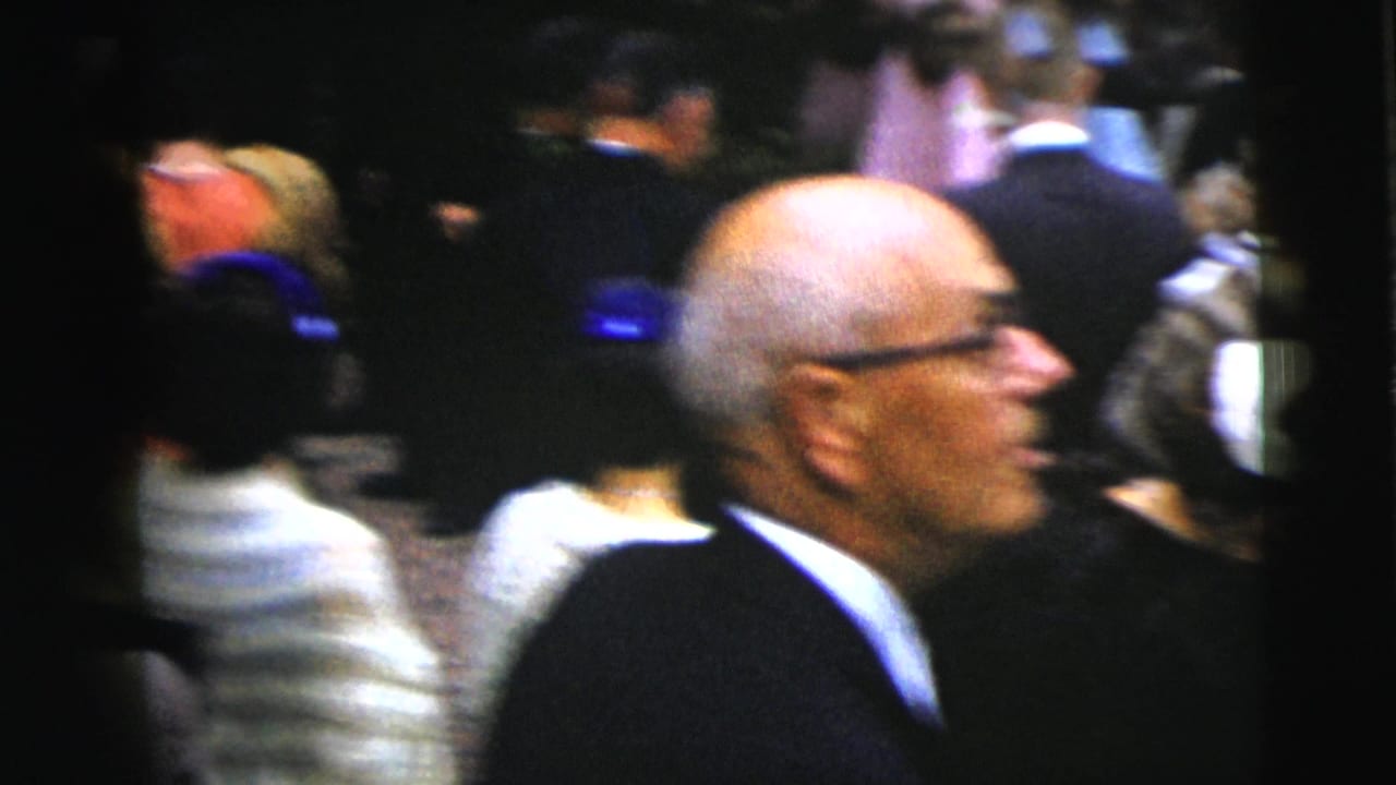 An older man in glasses is seen in profile among wedding guests.