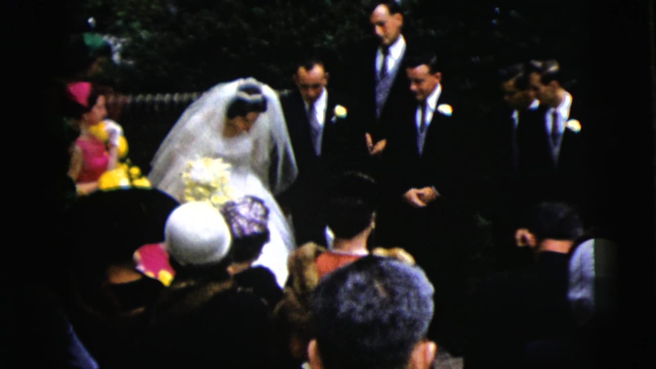 Bride in veil walks past seated wedding guests toward groomsmen.