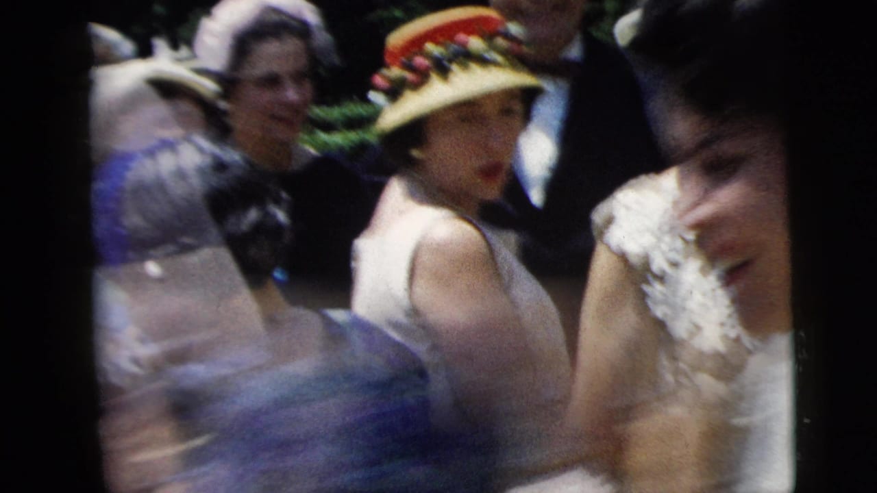Bride and wedding guests gathered closely outdoors, with a woman in a decorated hat facing the camera.