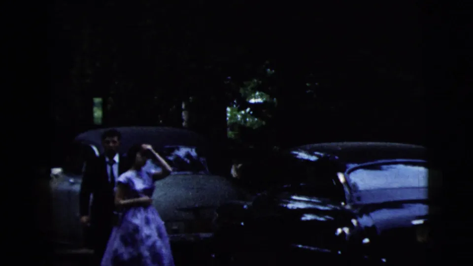 1962 Moline wedding frame showing the bride and groom near parked mid-century cars in a dim exterior scene.